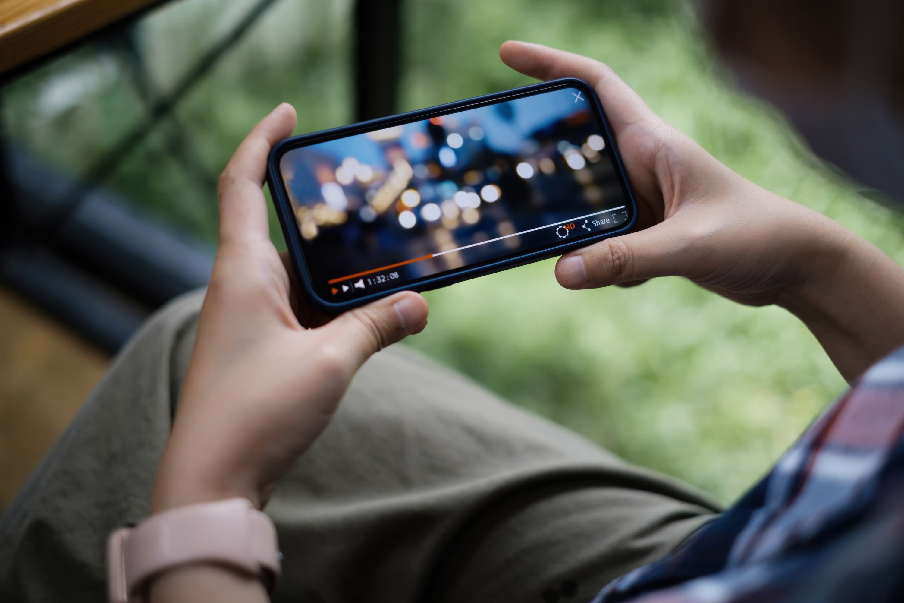 Hands of a person holding a cell phone horizontally watching a video.