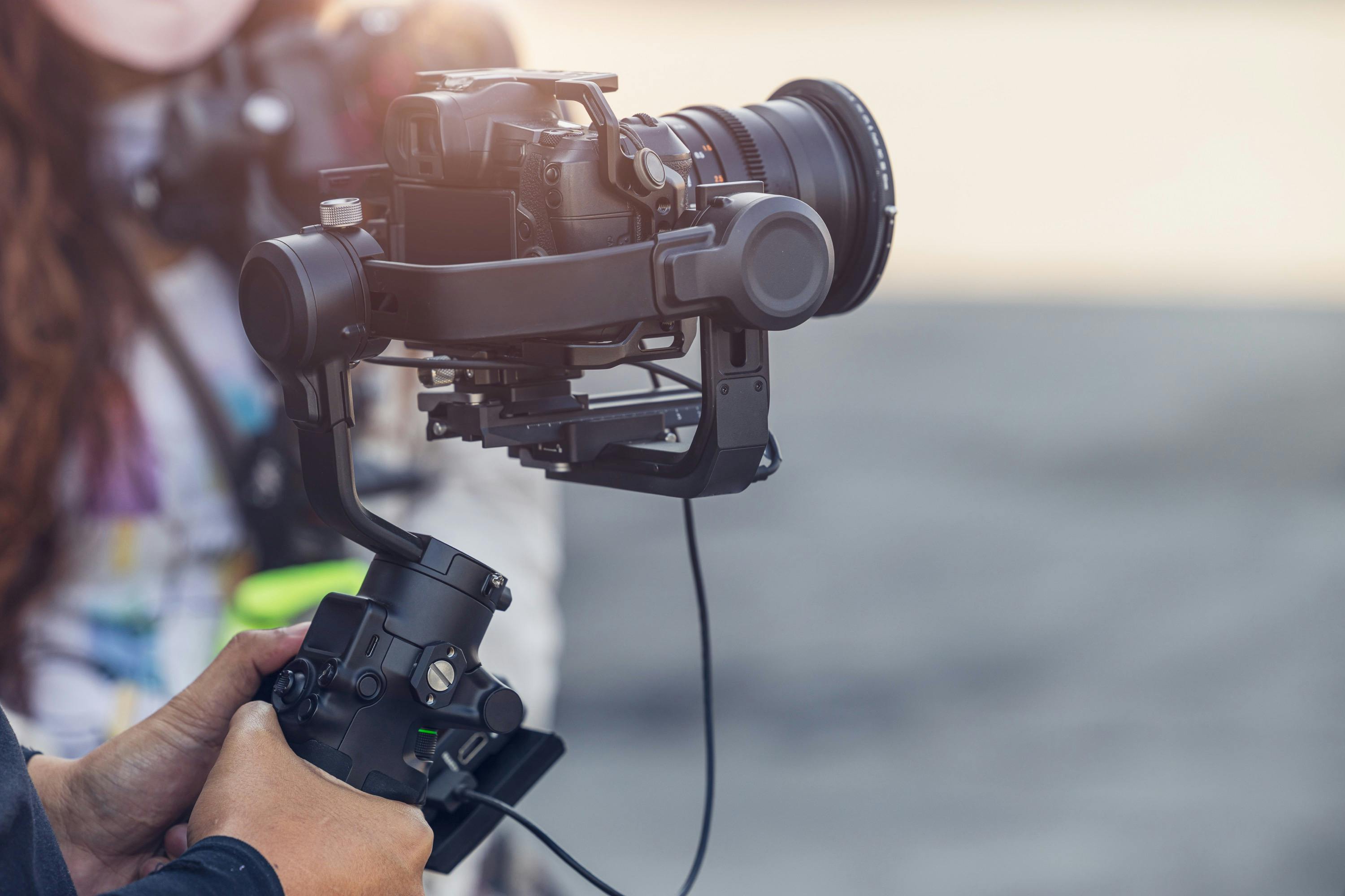 Hands of a person holding a gimbal stabilizer with a mirrorless camera attached.
